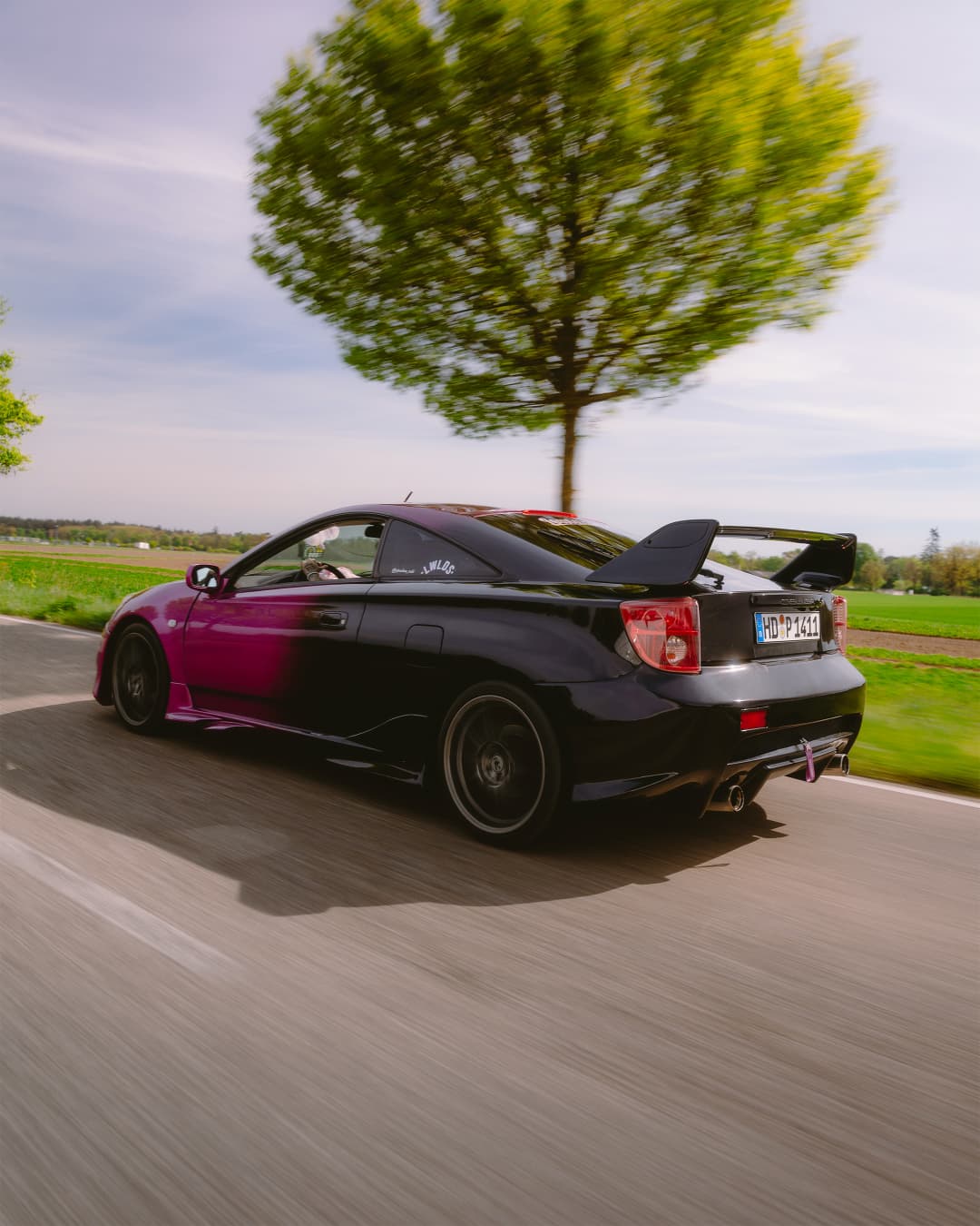 Toyota Celica Pink-Schwarz Heckansicht fahrend mit Heckspoiler